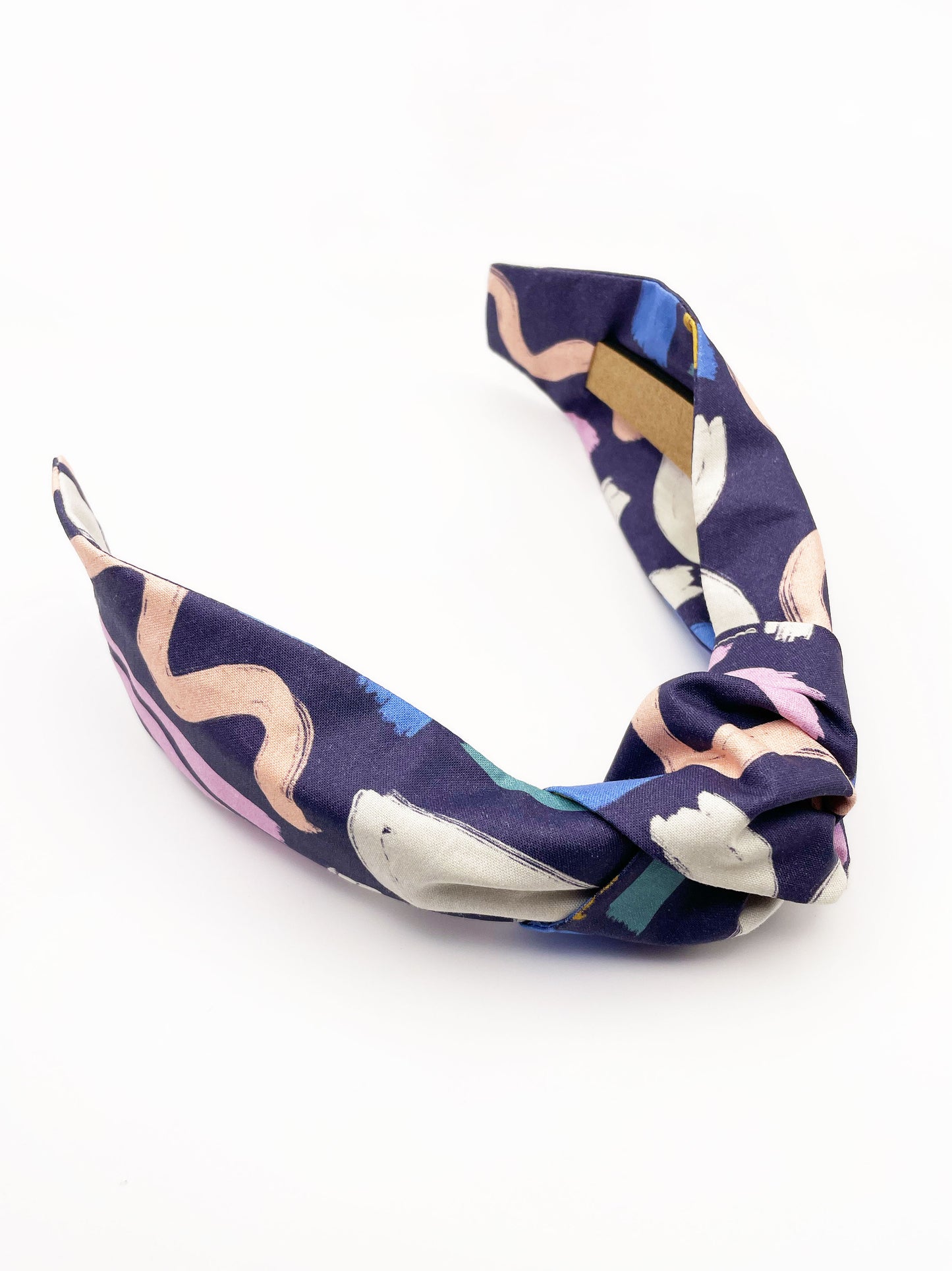 A navy blue knotted headband with a colorful abstract print featuring various doodles. Each headband is crafted with cotton fabric attached to a durable hair band for a secure and comfortable fit.