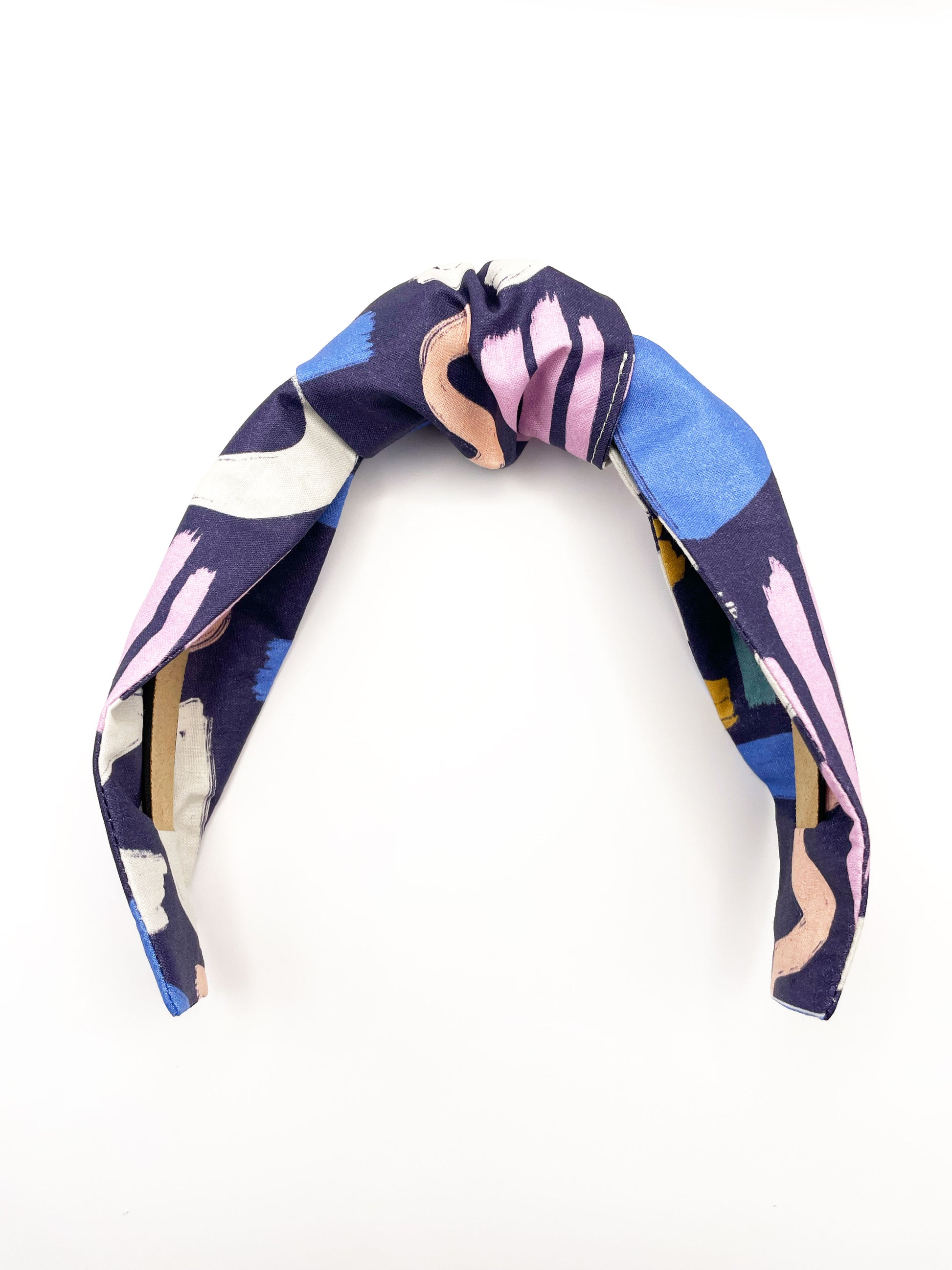 A navy blue knotted headband with a colorful abstract print featuring various doodles. Each headband is crafted with cotton fabric attached to a durable hair band for a secure and comfortable fit.