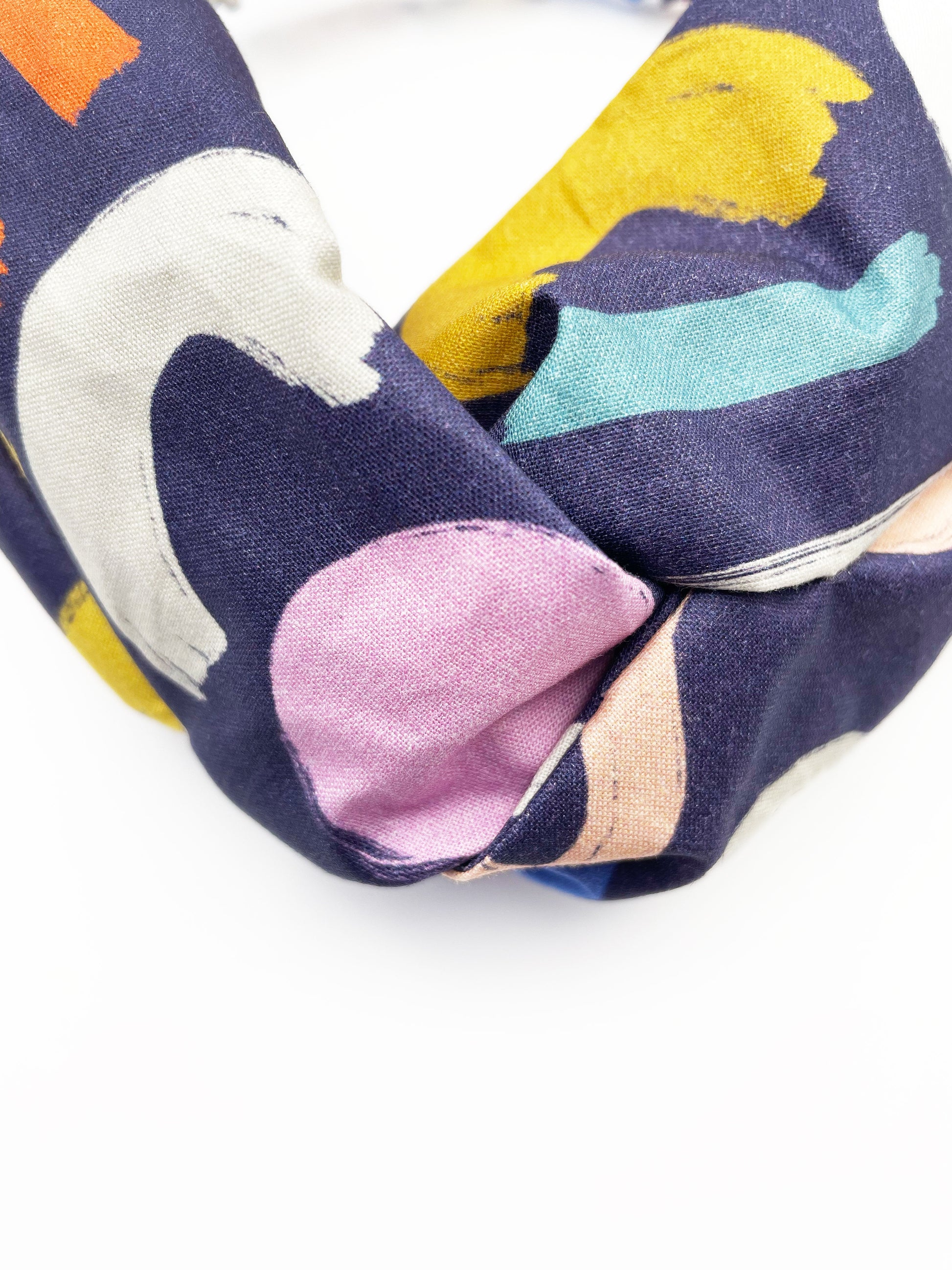 A navy blue twist headband with a colorful abstract print featuring various doodles. 