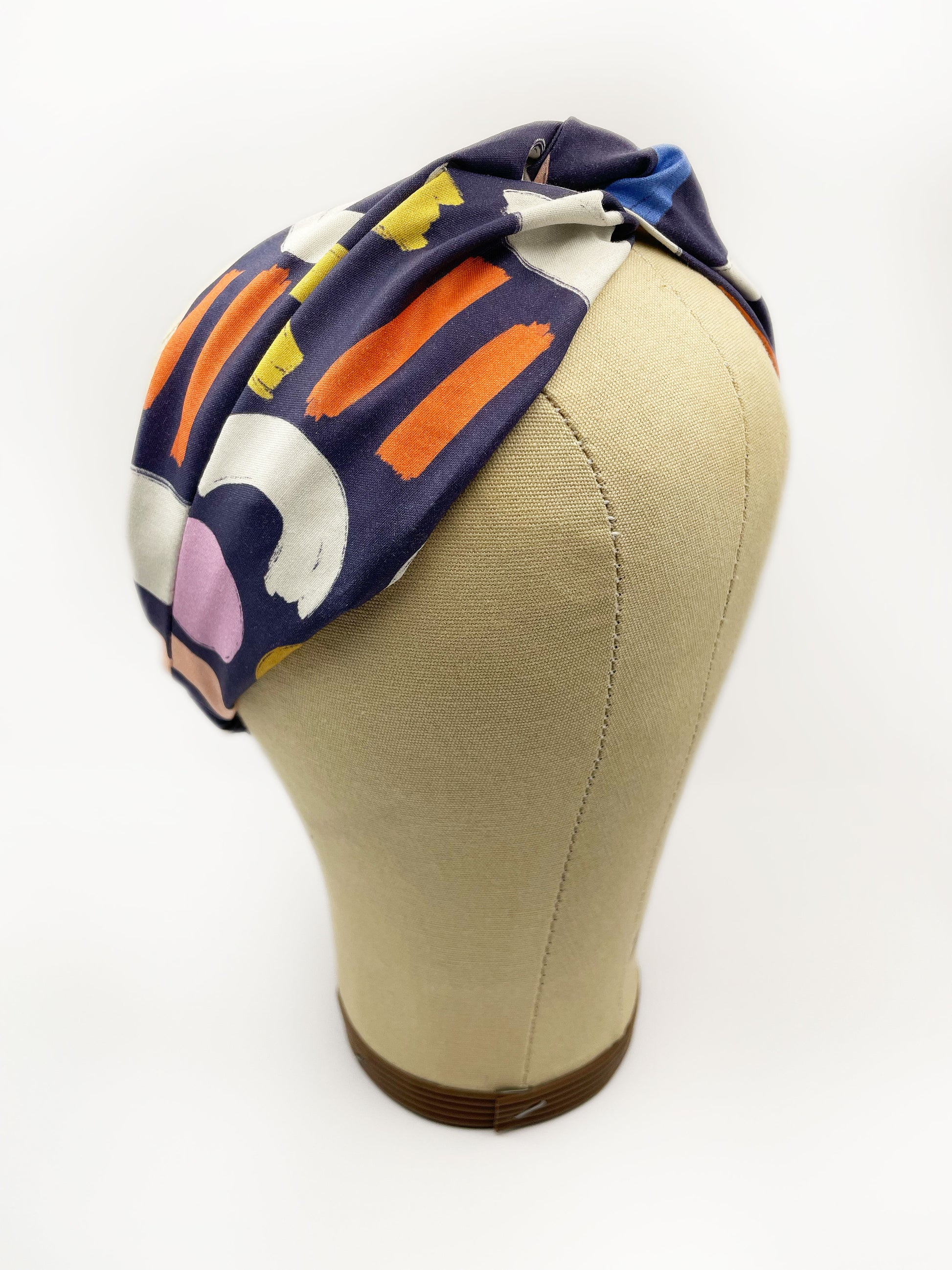 A navy blue twist headband with a colorful abstract print featuring various doodles. The headband is displayed on a mannequin head.