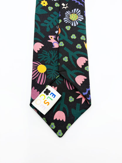 A necktie with an abstract print featuring bright forest creatures and flowers on a black background.