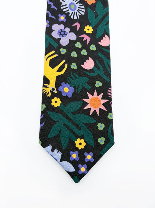 A necktie with an abstract print featuring bright forest creatures and flowers on a black background.
