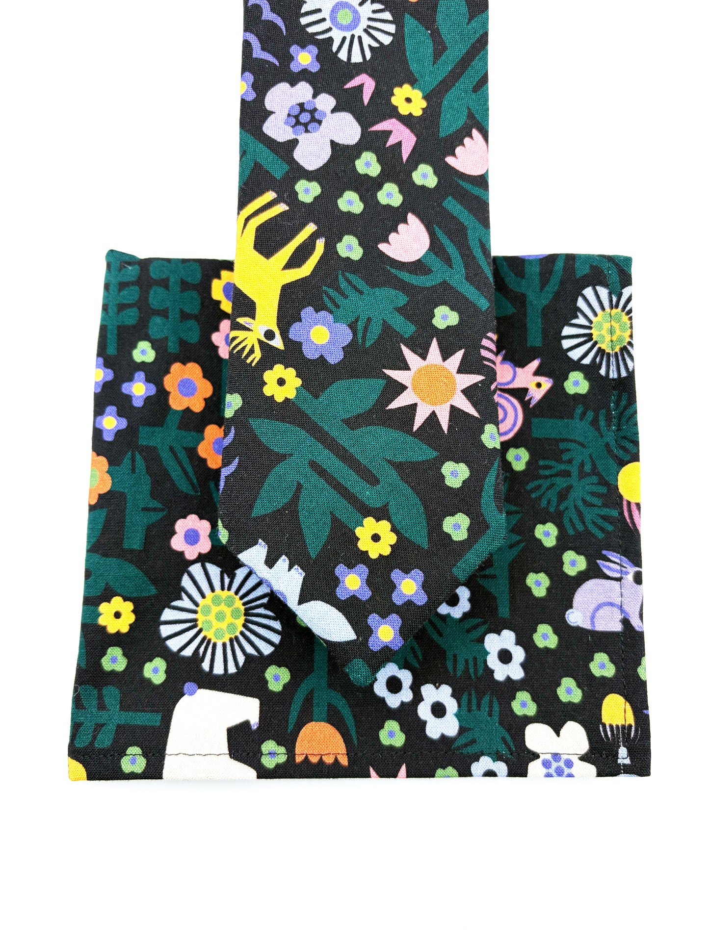 A necktie with an abstract print featuring bright forest creatures and flowers on a black background along with a matching pocket square.