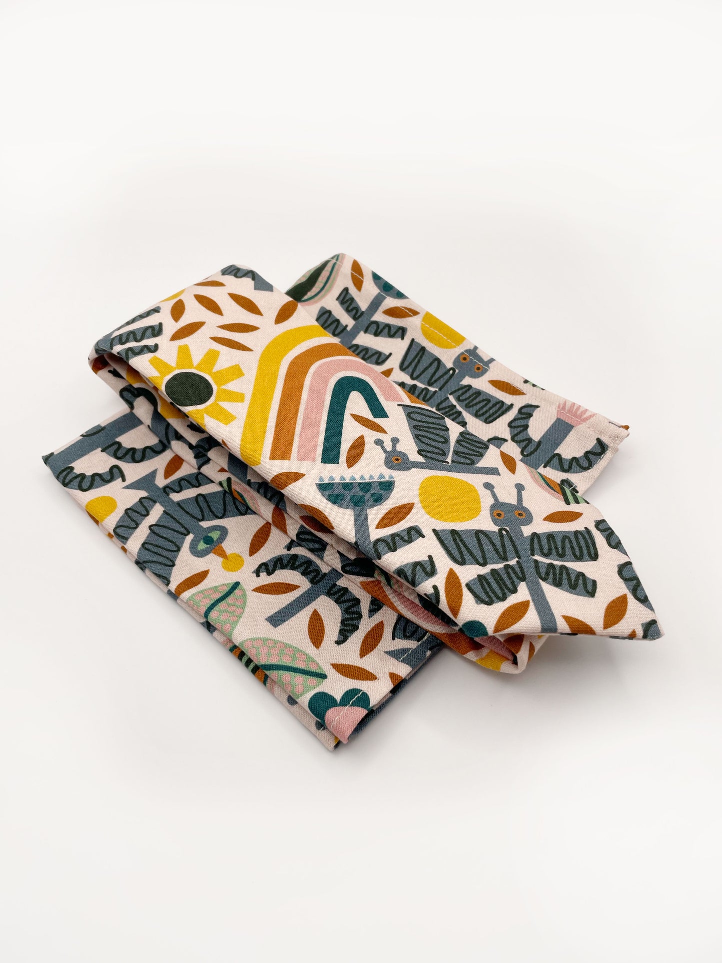 A necktie featuring a bold nature-inspired print of bugs, plants, suns, and rainbows. The color palette includes muted mustard, gentle gray, and soft pastels. The necktie is with a matching pocket square.