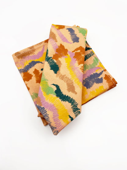 A pocket square crafted from high-quality cotton with an abstract design inspired by the rolling hills and earthy tones of the desert.  The square is shown with a matching necktie. 