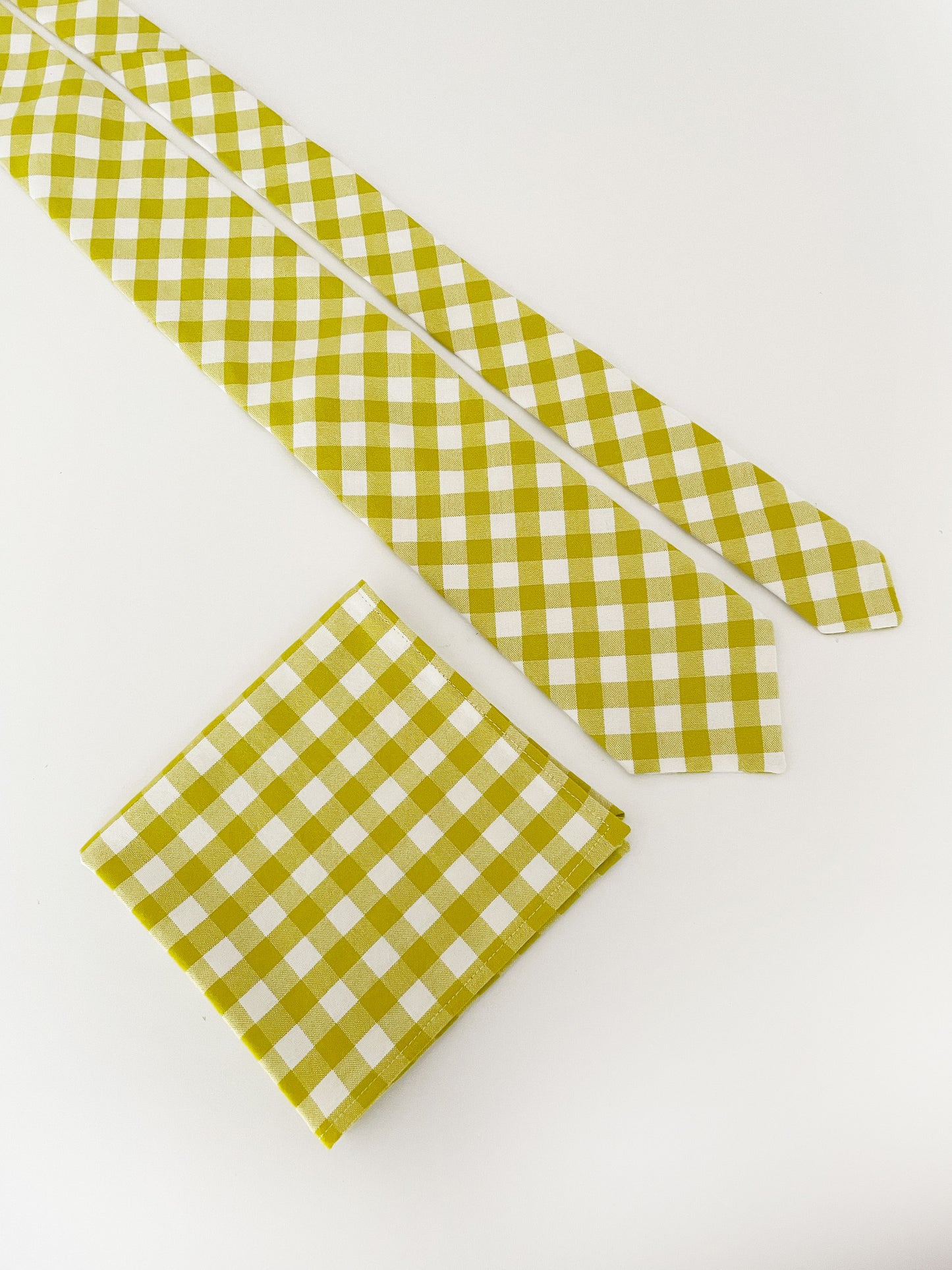 A cotton handmade pocket square with a green gingham plaid print. The pocket square is shown with a matching necktie (sold separately).