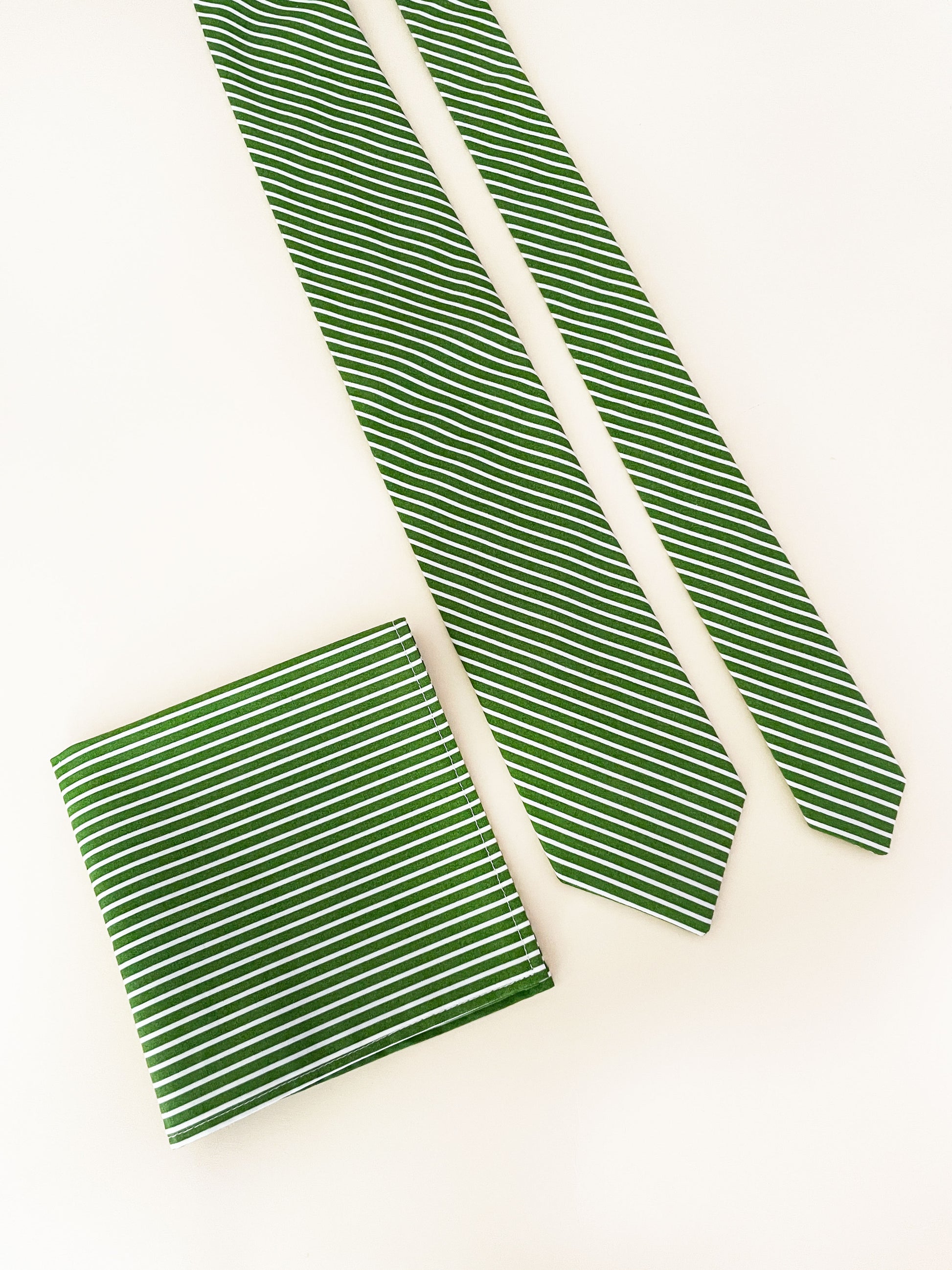 A handmade green necktie with white stripes next to a matching pocket square.