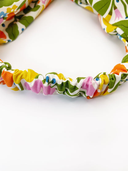 A vibrant twist headband with bold yellow, orange, and pink flowers. The elastic band in the back provides support without slipping.