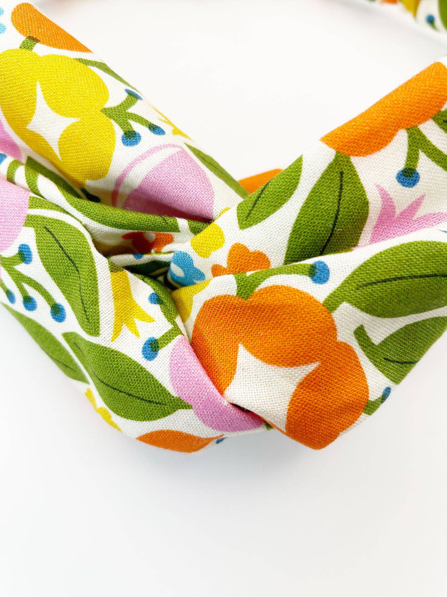 A vibrant twist headband with bold yellow, orange, and pink flowers.