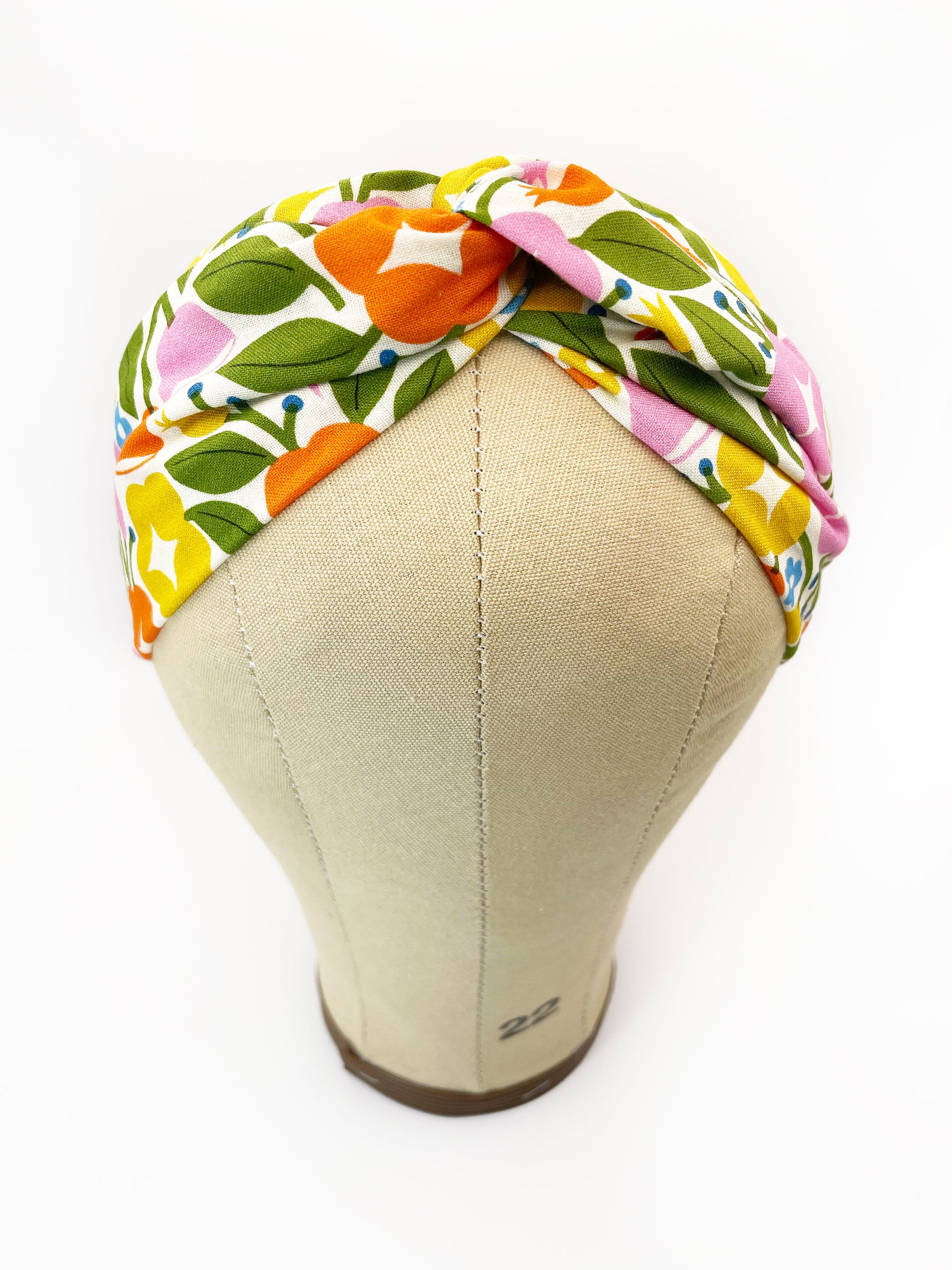 A vibrant twist headband with bold yellow, orange, and pink flowers. The headband is modeled on a mannequin head.