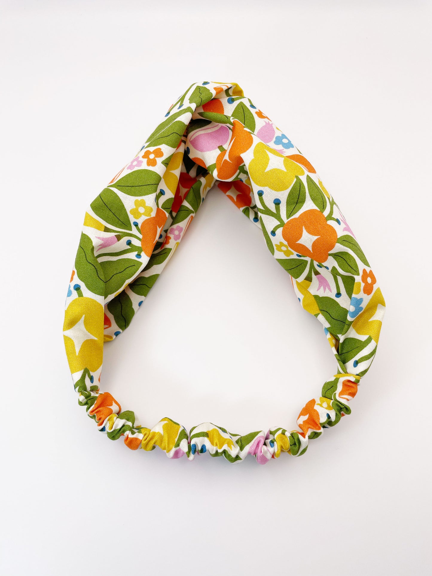 A vibrant twist headband with bold yellow, orange, and pink flowers. The elastic band in the back provides support without slipping.