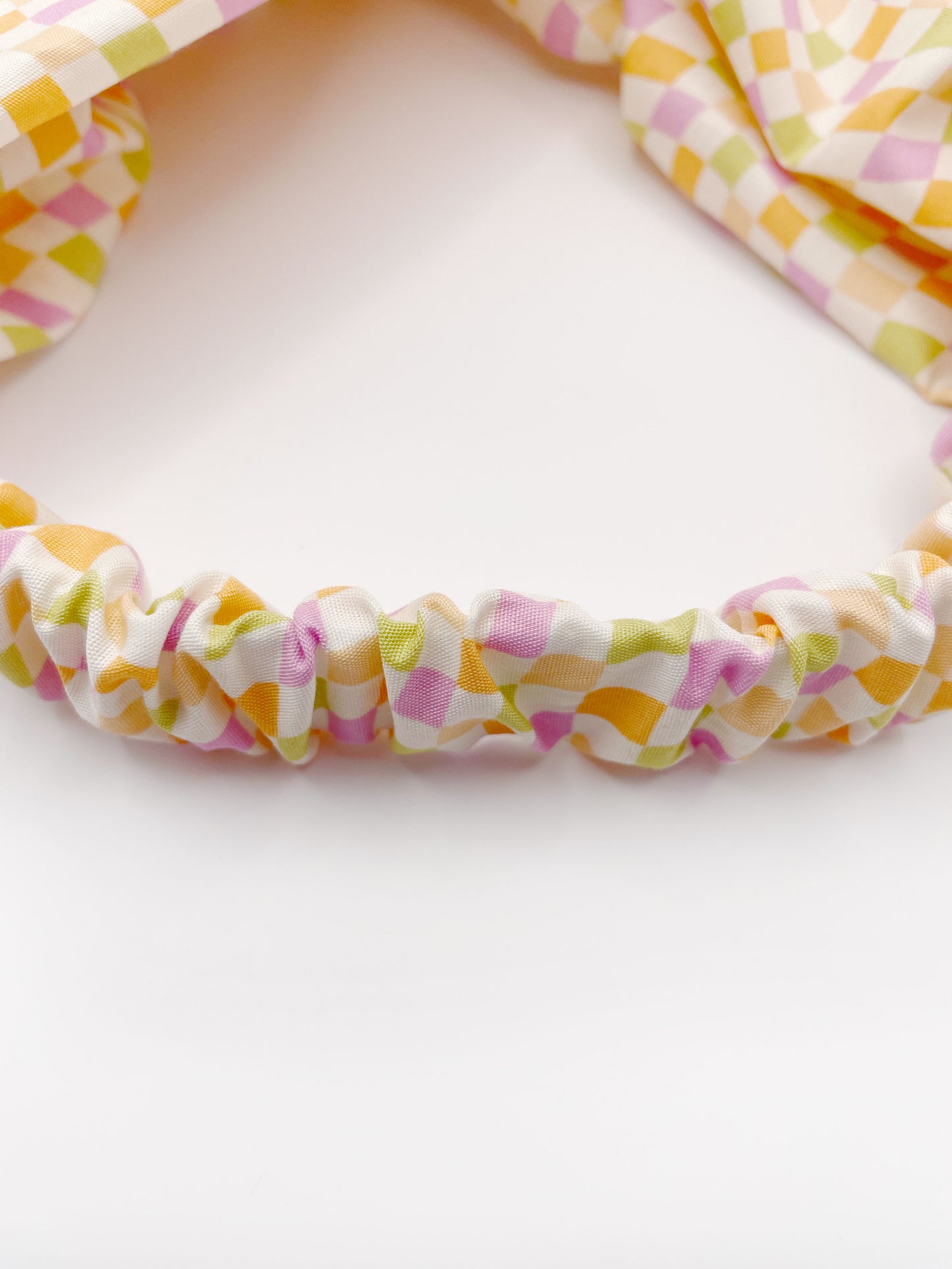 A handmade twist headband with a pastel checkered print. The headband has an elastic band.