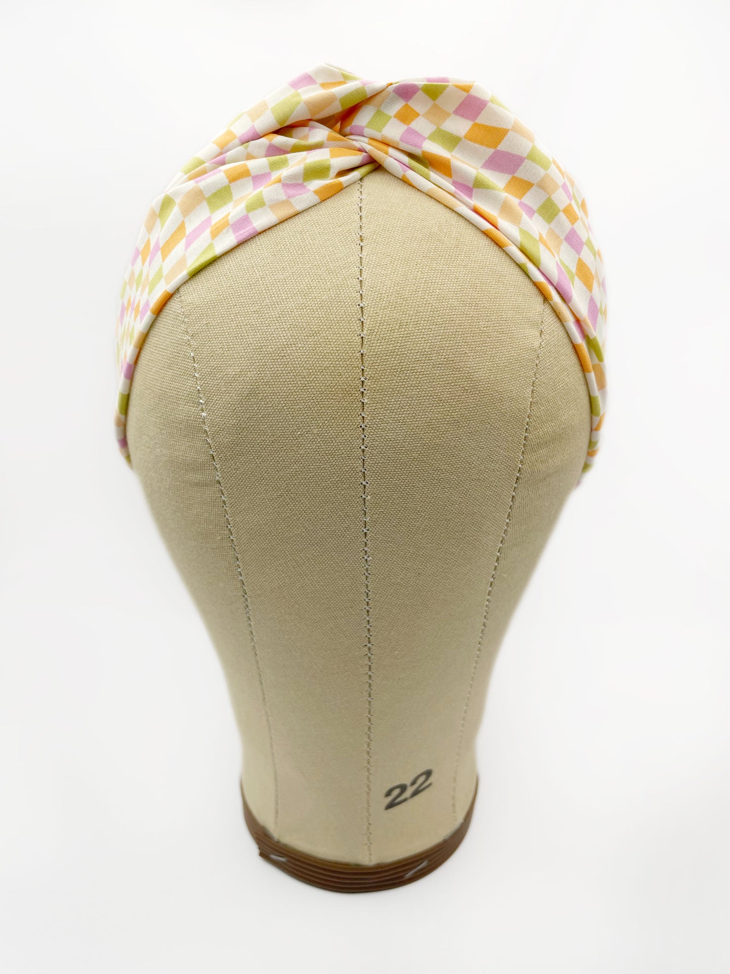 A handmade twist headband with a pastel checkered print. The headband is displayed on a mannequin head.