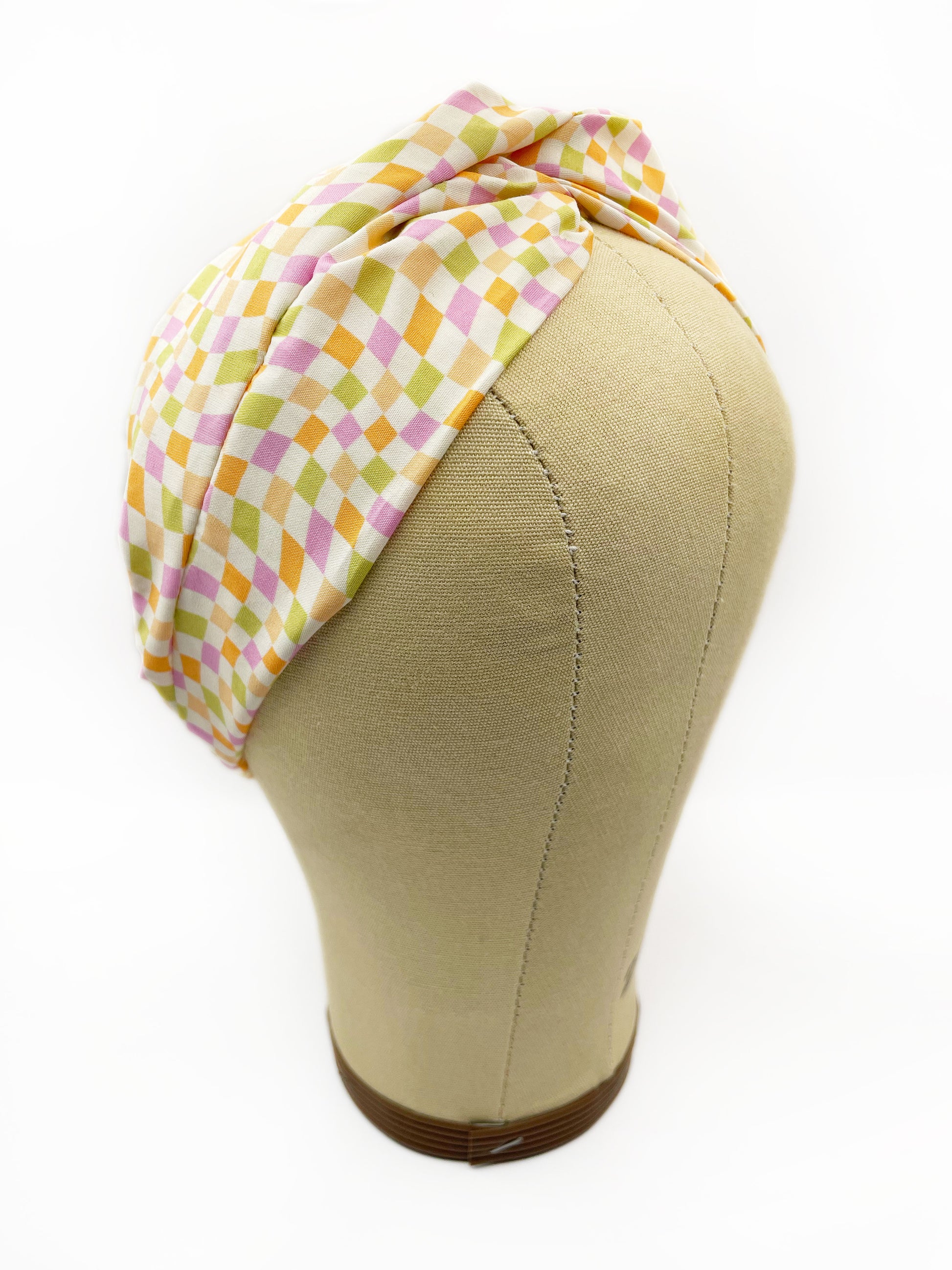 A handmade twist headband with a pastel checkered print. The headband is displayed on a mannequin head.