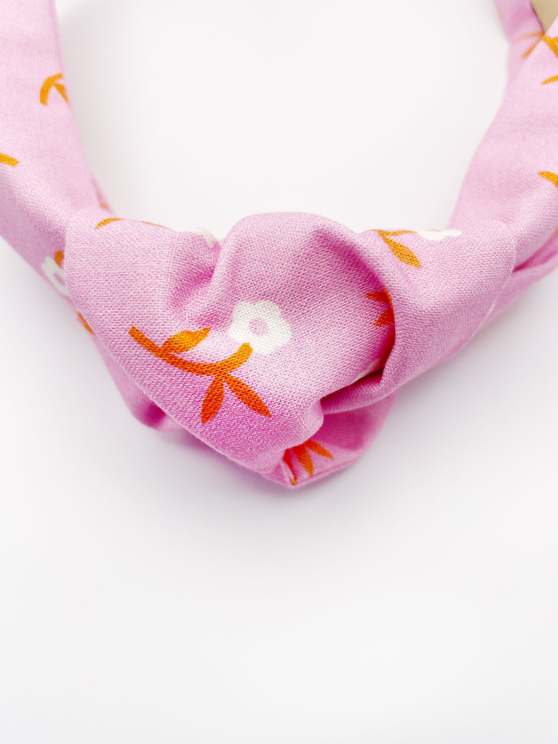 A cheerful pink knotted headband with orange-stemmed flowers. 