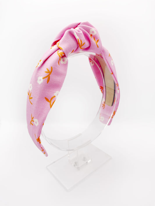 A cheerful pink knotted headband with orange-stemmed flowers. 