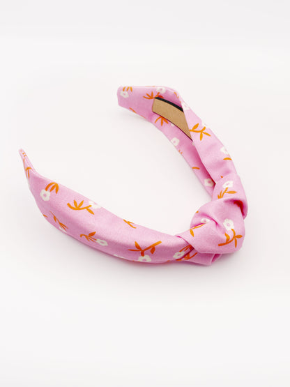 A cheerful pink knotted headband with orange-stemmed flowers. 