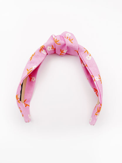 A cheerful pink knotted headband with orange-stemmed flowers. 