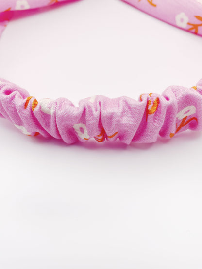 A cheerful pink twist headband with orange-stemmed flowers. The elastic band in the back provides support without slipping.