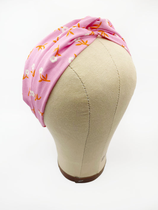 A cheerful pink twist headband with orange-stemmed flowers. The headband is modeled on a mannequin head.
