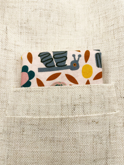 A pocket square featuring a bold nature-inspired print of bugs, plants, suns, and rainbows.