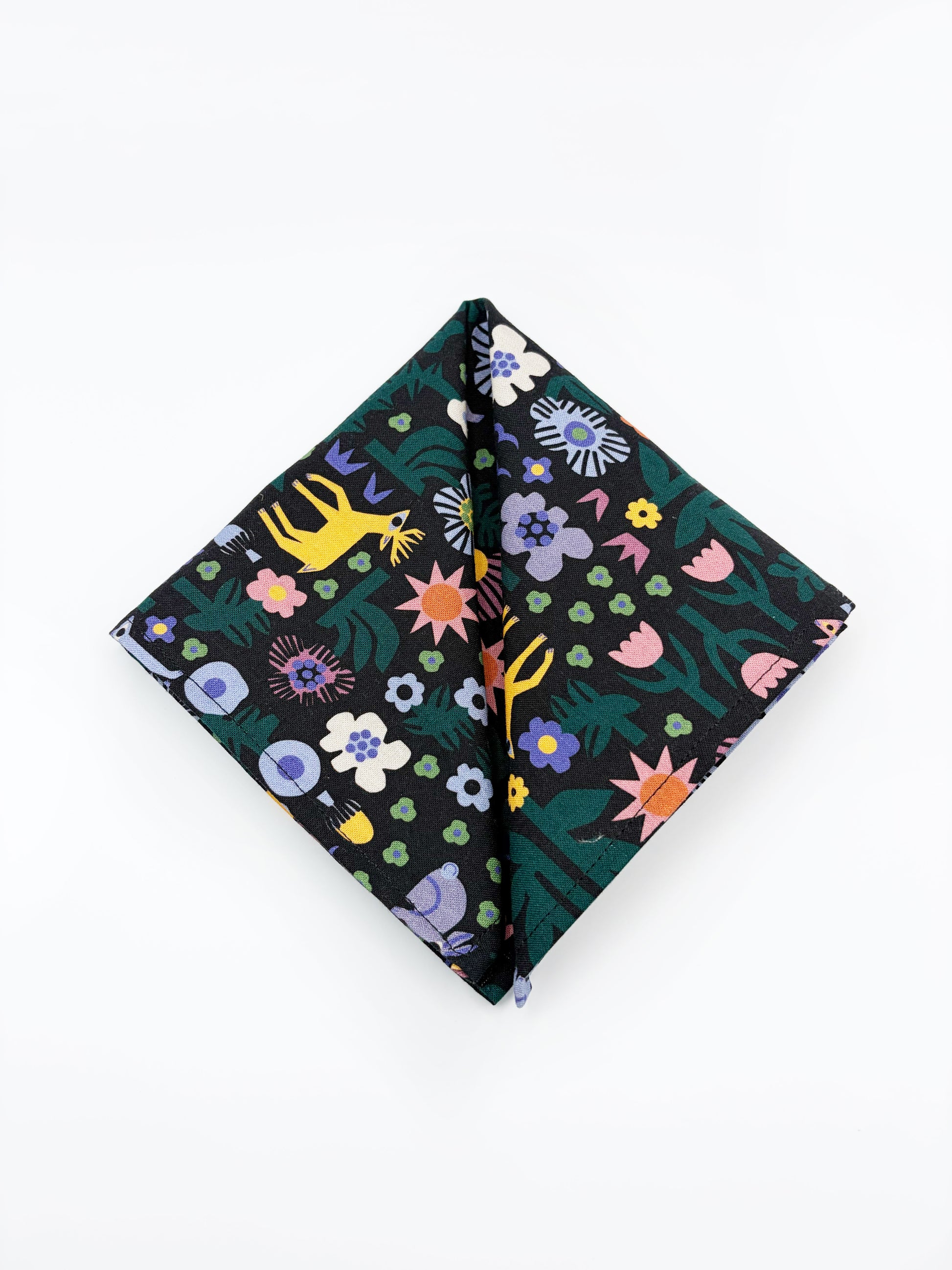 A black pocket square with a colorful abstract forest print featuring playful florals, leaves, and bright animals.
