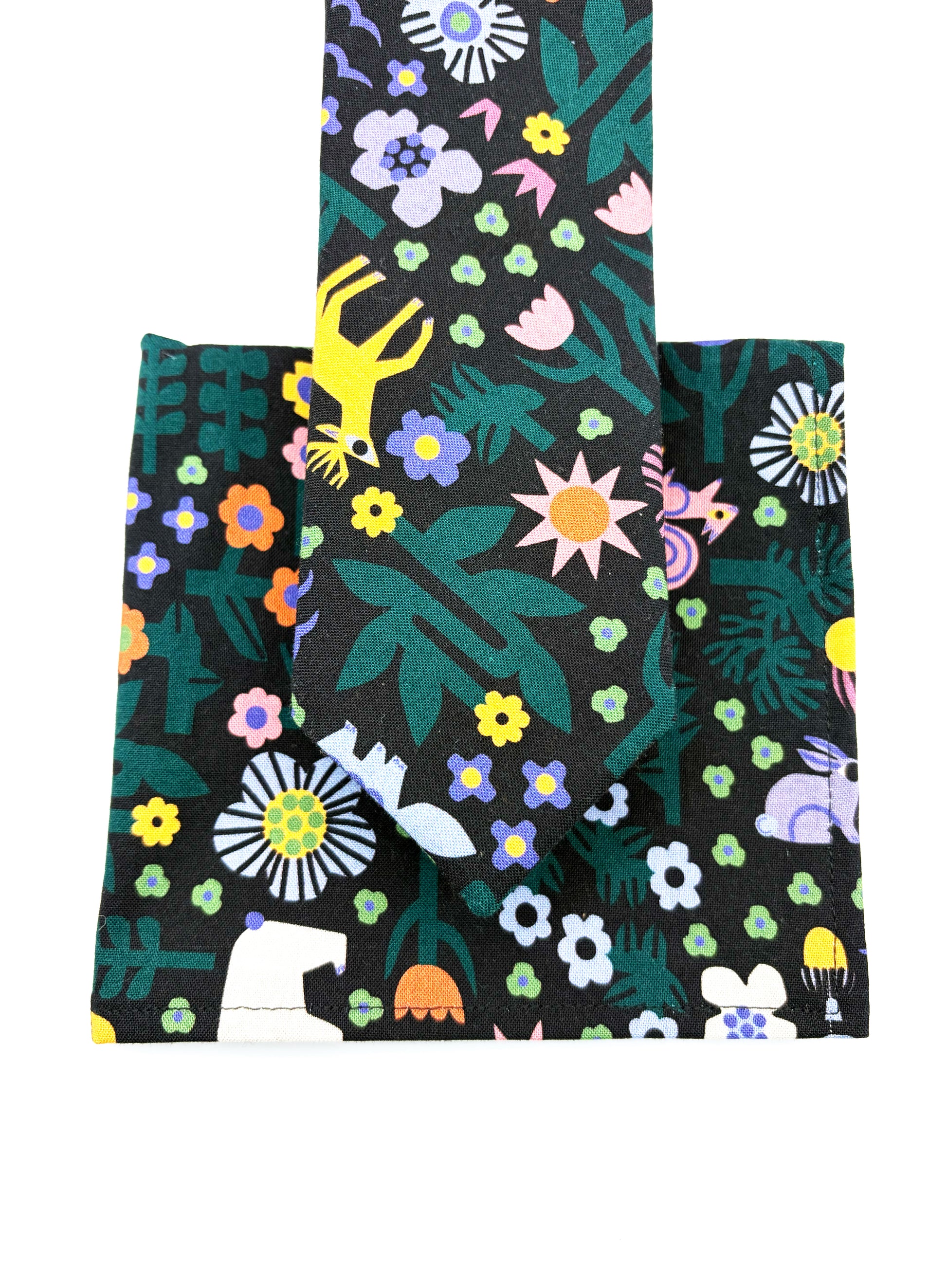 A black pocket square with a colorful abstract forest print featuring playful florals, leaves, and bright animals. The pocket square is shown with a matching necktie.
