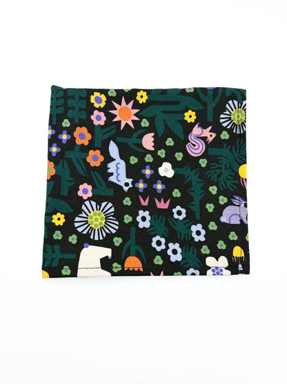 A black pocket square with a colorful abstract forest print featuring playful florals, leaves, and bright animals.