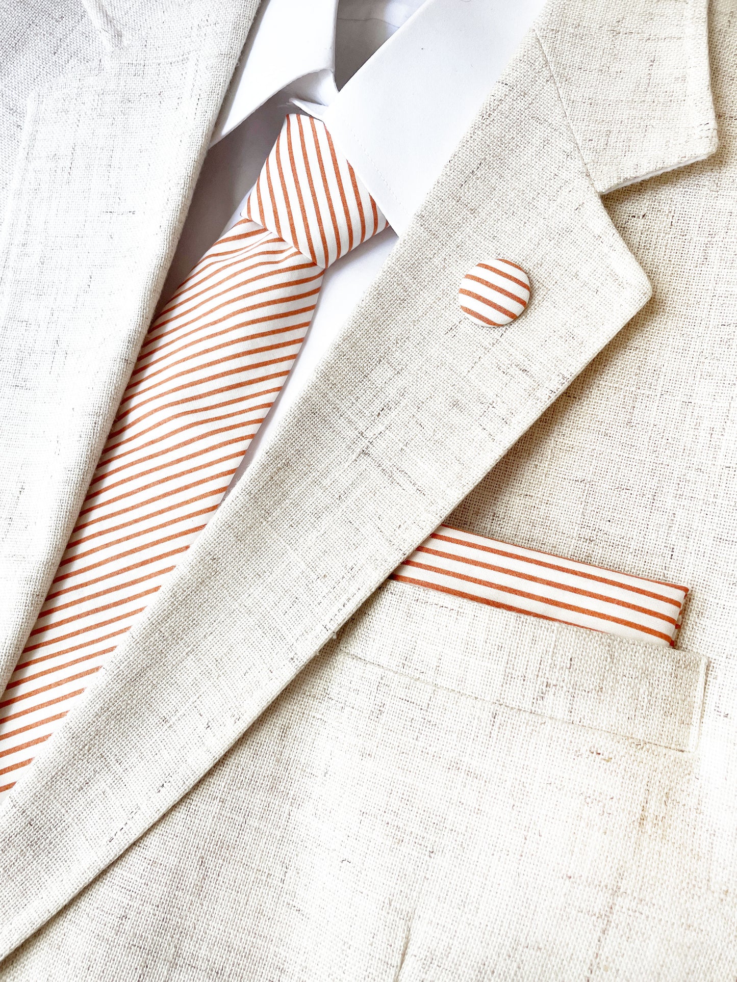 A handmade pocket square with copper stripes, along with a matching necktie and lapel pin.