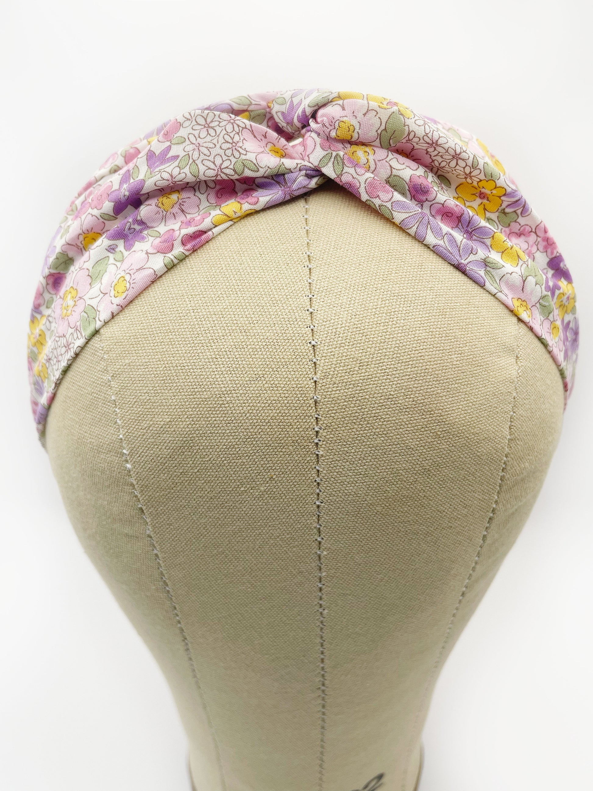 A handmade twist headband with purple flowers. The headband is modeled on a mannequin head.