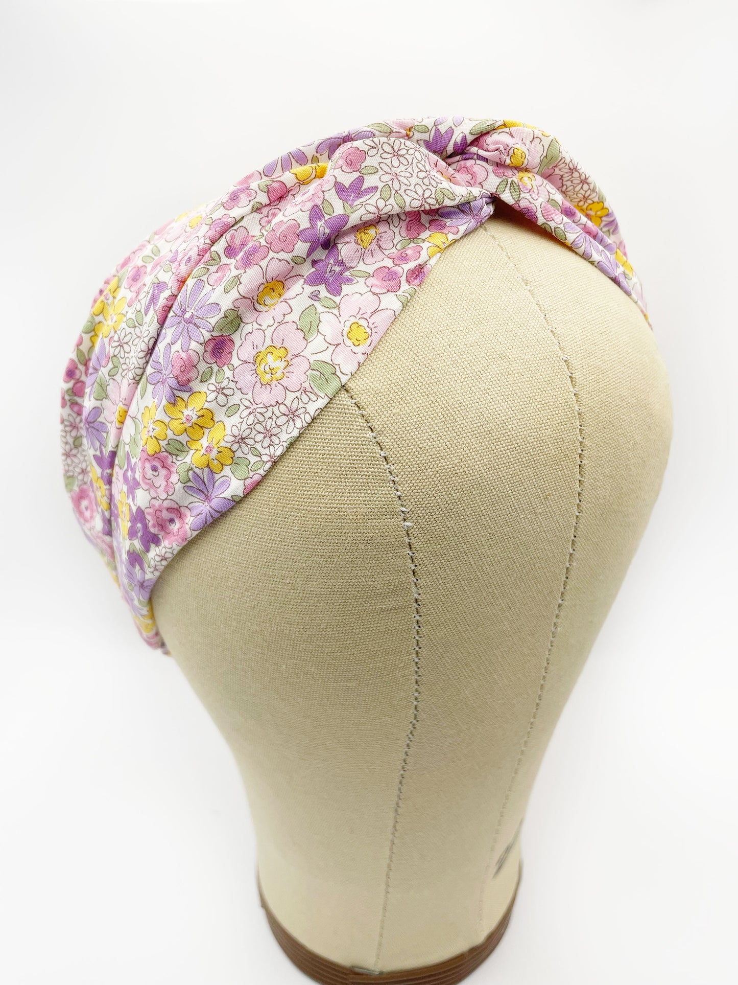 A handmade twist headband with purple flowers. The headband is modeled on a mannequin head.