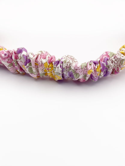 A handmade twist headband with purple flowers. The headband has an elastic band in the back.