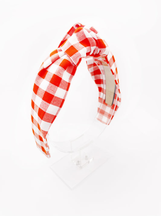 Cotton knotted headbands with a vibrant red gingham plaid print. The headband is displayed on an acrylic stand.