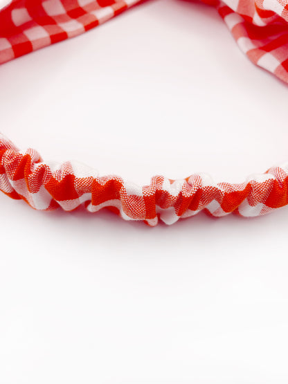 A cotton twist headband with a vibrant red gingham plaid print. The headband has an elastic band in the back.