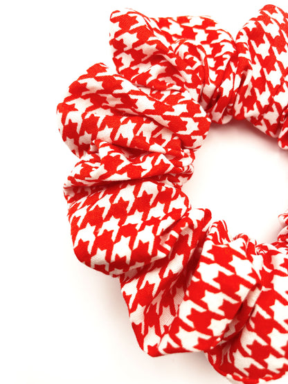 A handmade scrunchie made with cotton fabric featuring a vibrant red houndstooth print. 