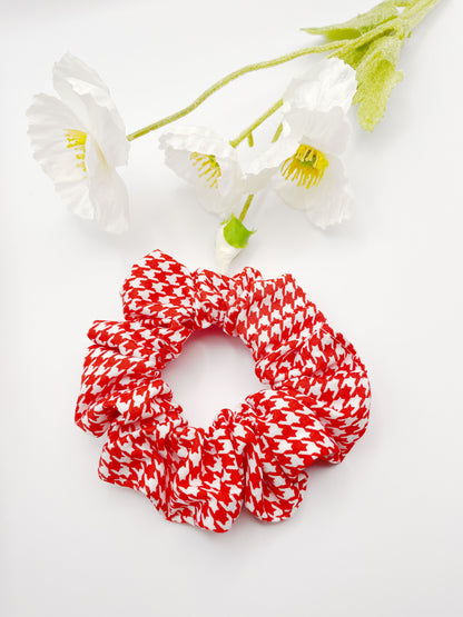 A handmade scrunchie made with cotton fabric featuring a vibrant red houndstooth print. 