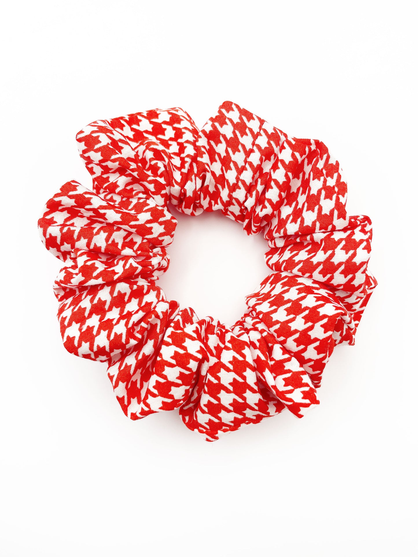 A handmade scrunchie made with cotton fabric featuring a vibrant red houndstooth print. 