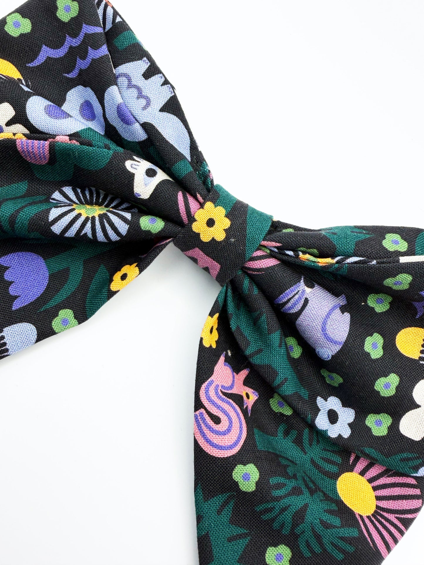 A black hair bow with a colorful abstract forest print featuring playful florals, leaves, and bright animals. 