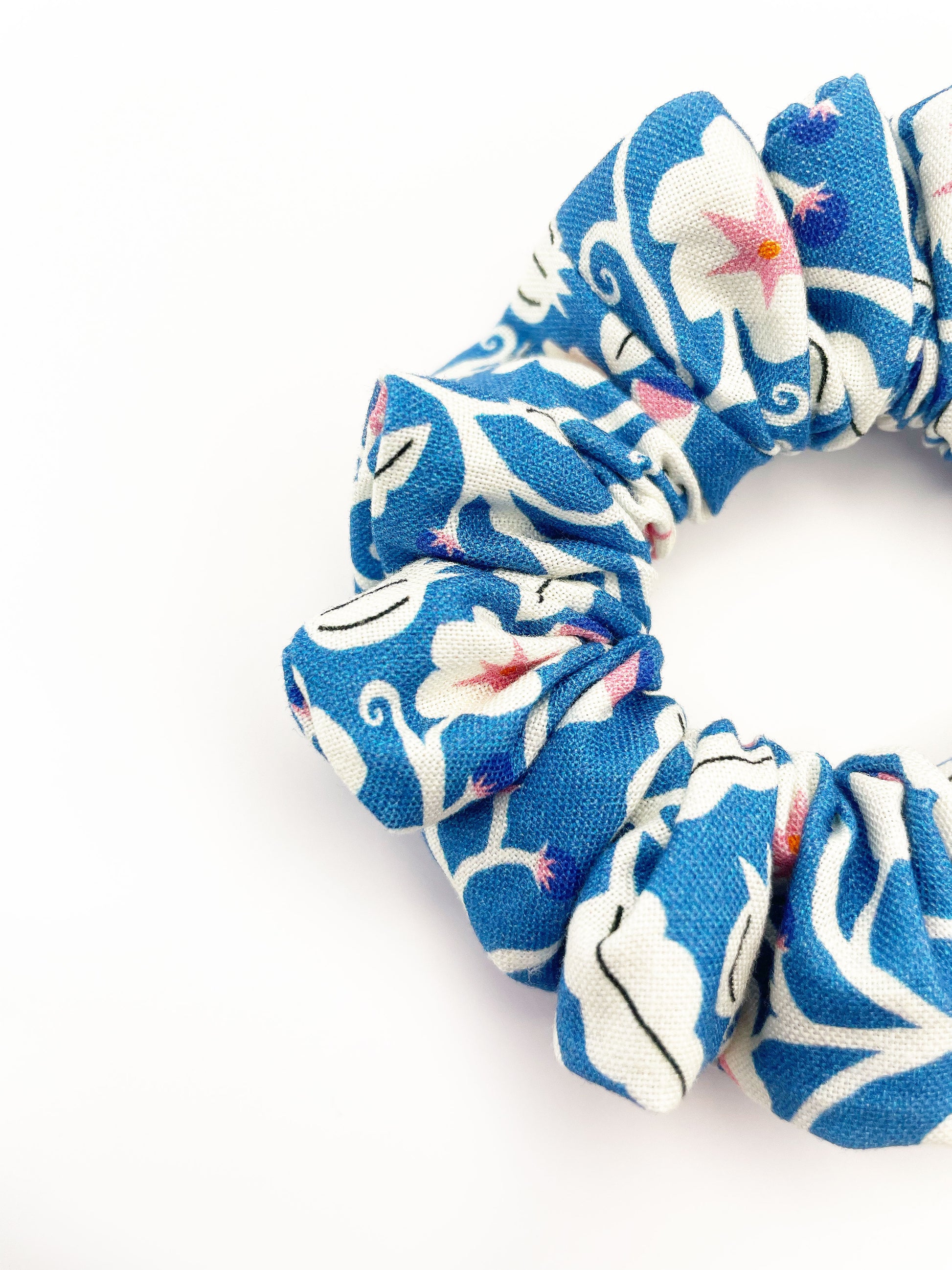 A closeup of a blue scrunchie with white flowers that have pink centers.