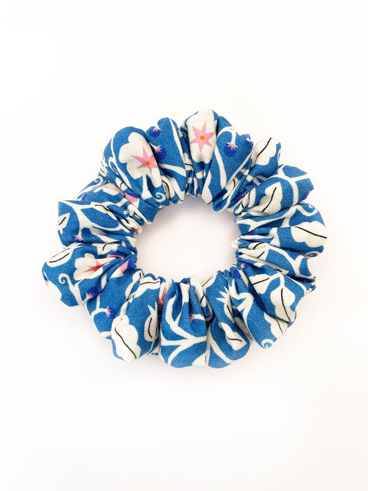 A blue scrunchie with white flowers that have pink centers.