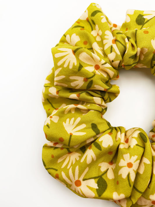 A handmade scrunchie showcasing shades of moss green, earthy browns, and pops of warm peach and blush pink. 