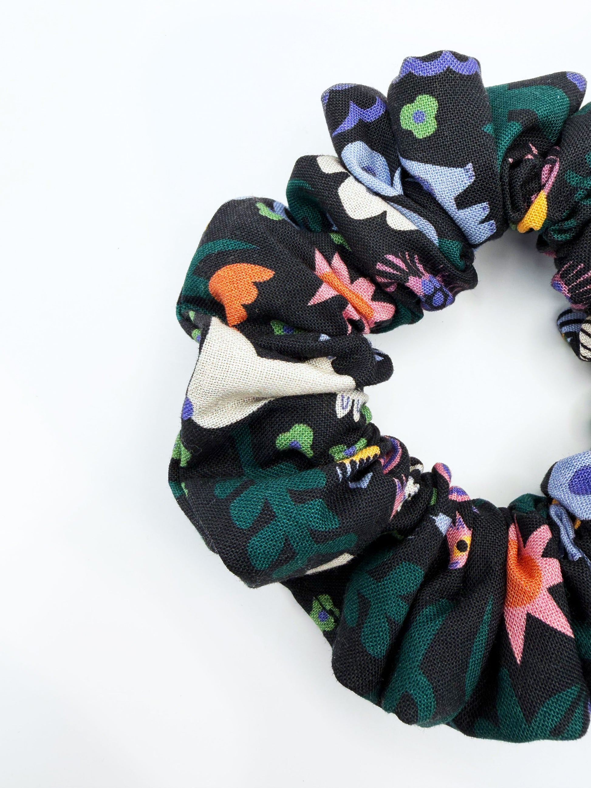 A black scrunchie with a colorful abstract forest print featuring playful florals, leaves, and bright animals.