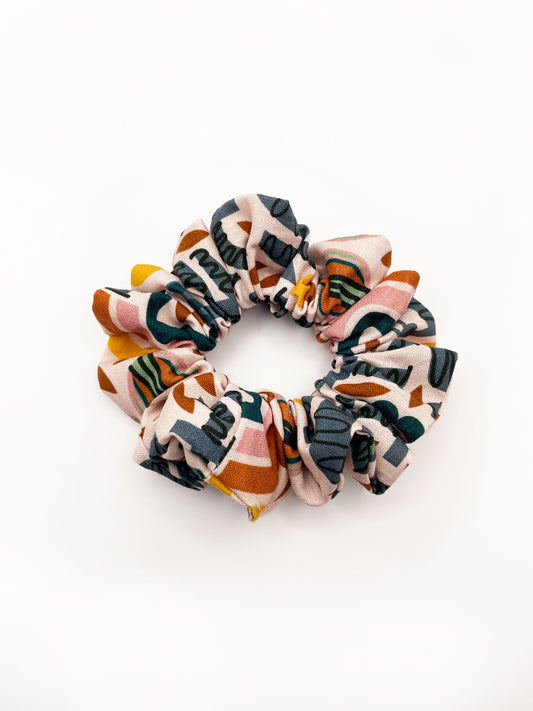 A scrunchie featuring a bold nature-inspired print of bugs, plants, suns, and rainbows.