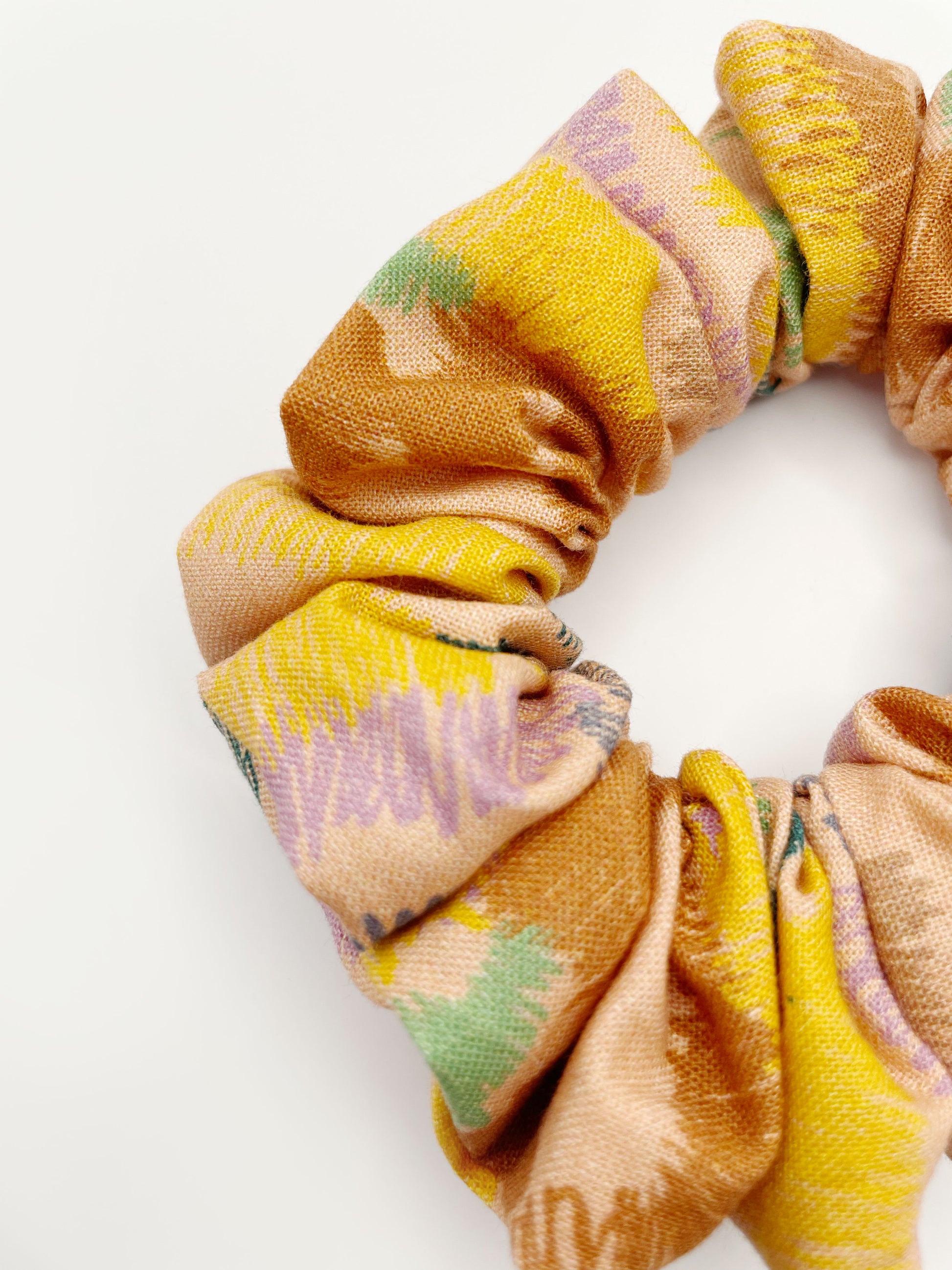 A scrunchie crafted from high-quality cotton with an abstract design inspired by the rolling hills and earthy tones of the desert. 