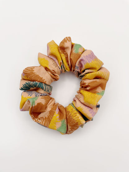 A scrunchie crafted from high-quality cotton with an abstract design inspired by the rolling hills and earthy tones of the desert. 