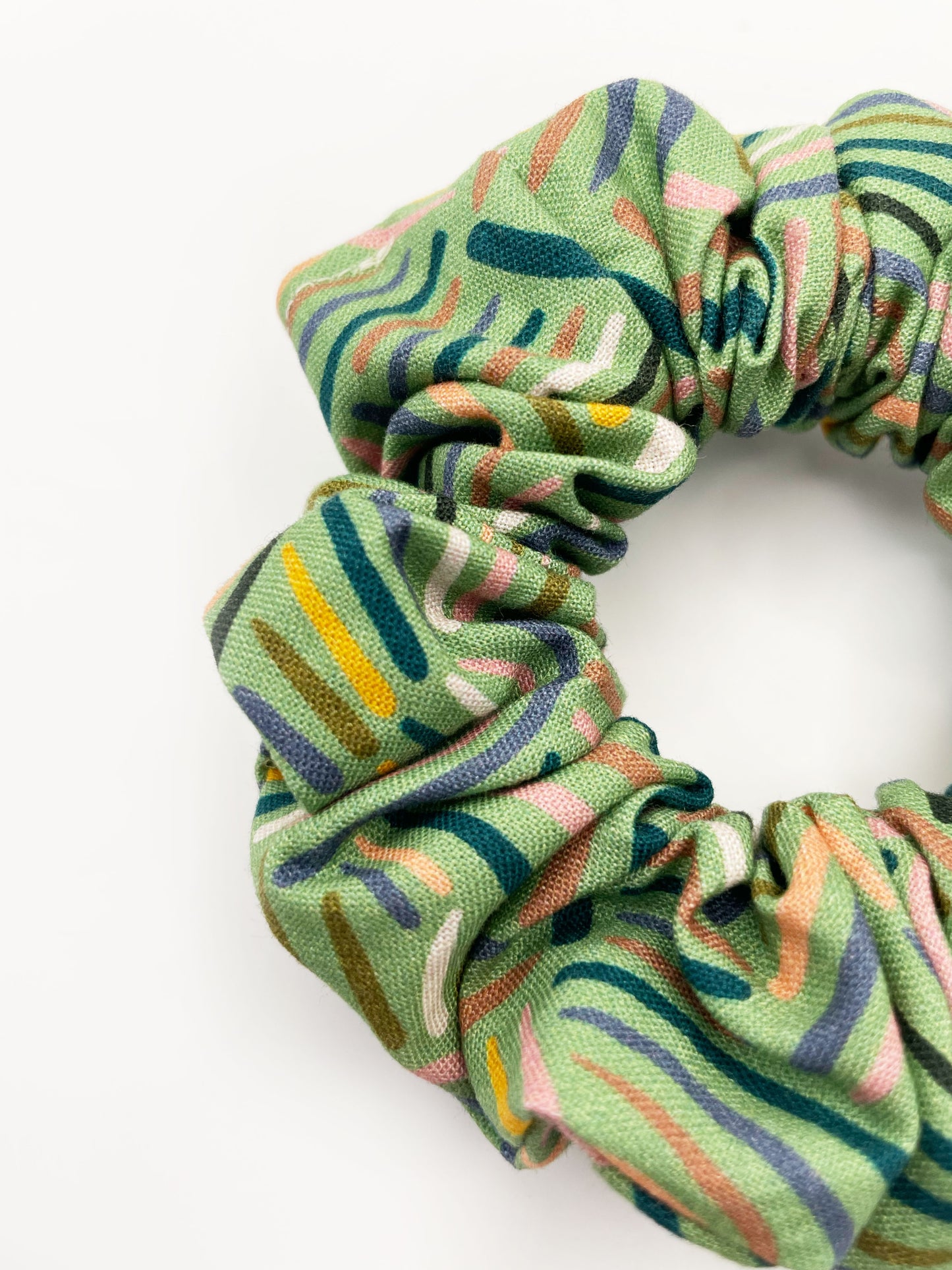 A scrunchie made from high-quality cotton with an abstract design inspired by desert rain patterns.