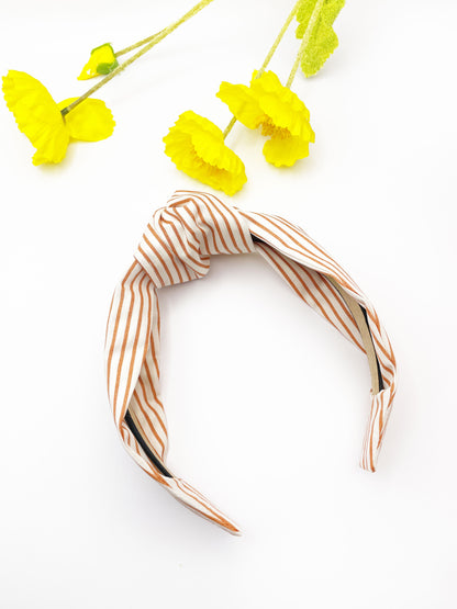 A handmade copper striped knotted headband next to yellow flowers.