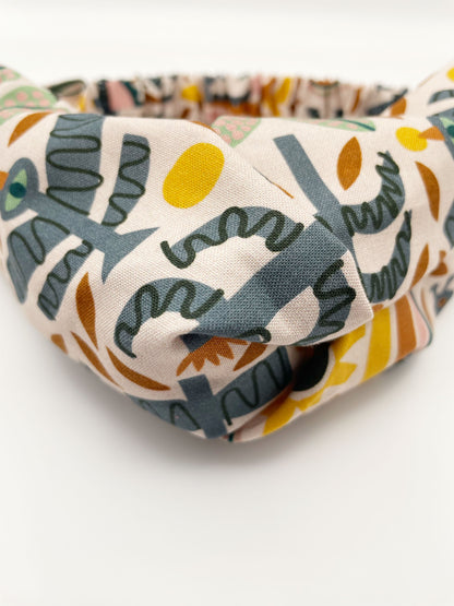 A twist headband featuring a bold nature-inspired print of bugs, plants, suns, and rainbows. 