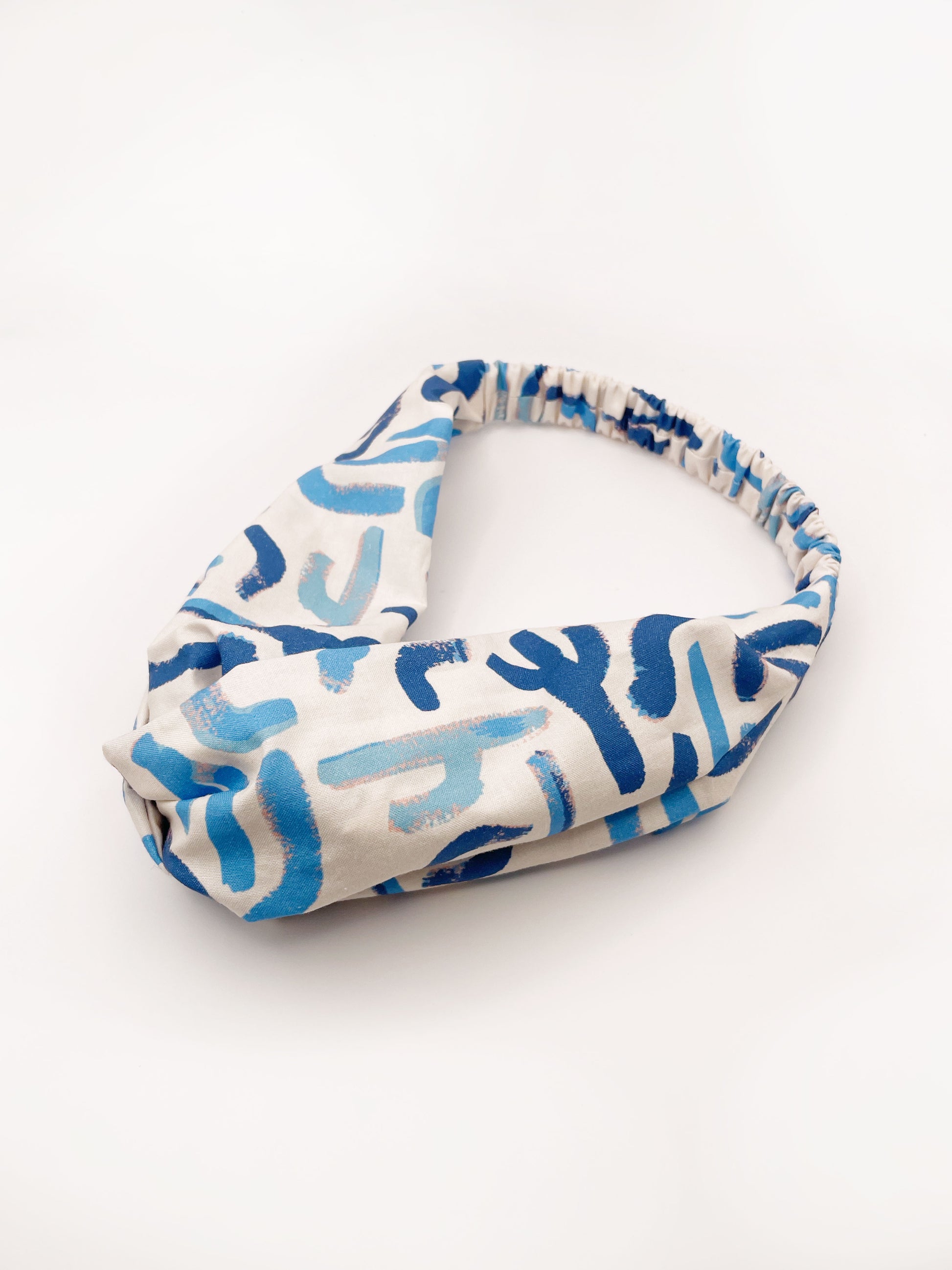 A twist headband featuring a bold blue cactus print. The headband has an elastic band on the back.