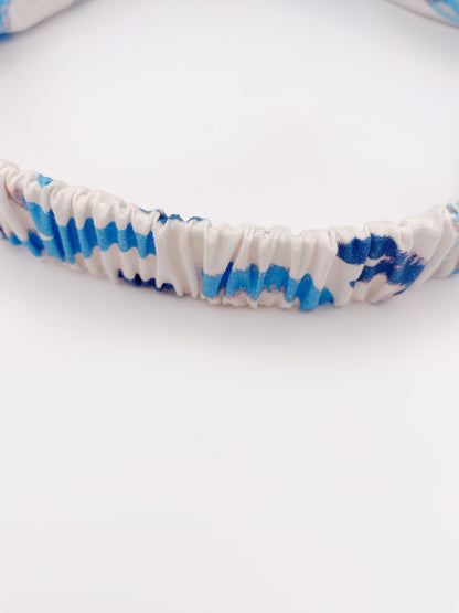 A twist headband featuring a bold blue cactus print. The headband has an elastic band on the back.